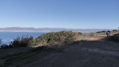 motociclista de aventuras pasa por un camino de ripio con vistas al mar y a la ciudad de baja california, méxico