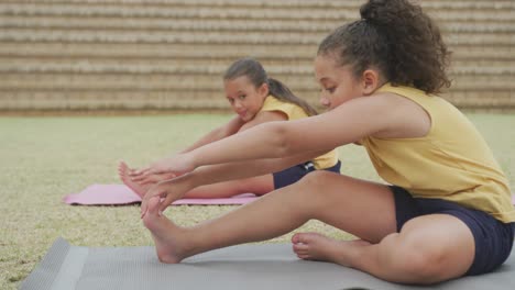 video of focused diverse girls stretching on mats in front of school