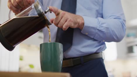 Midsection-of-caucasian-man-wearing-tie,-standing-in-kitchen-and-making-coffee