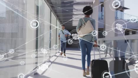 Animation-of-connected-globe-and-graph-icons-over-diverse-man-running-and-woman-walking-in-corridor