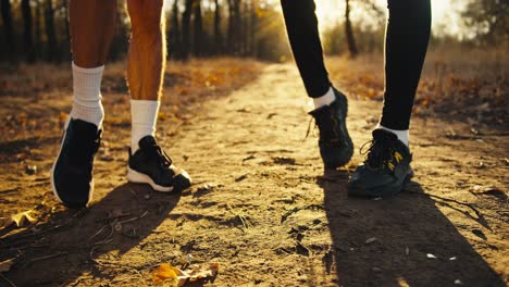 Primer-Plano-De-Una-Pareja-De-Amigos-Con-Zapatillas-Negras-Y-Calcetines-Blancos-Estiran-Los-Pies-Antes-De-Empezar-A-Trotar-Por-Un-Sendero-De-Tierra-En-Un-Parque-Otoñal-Al-Amanecer.