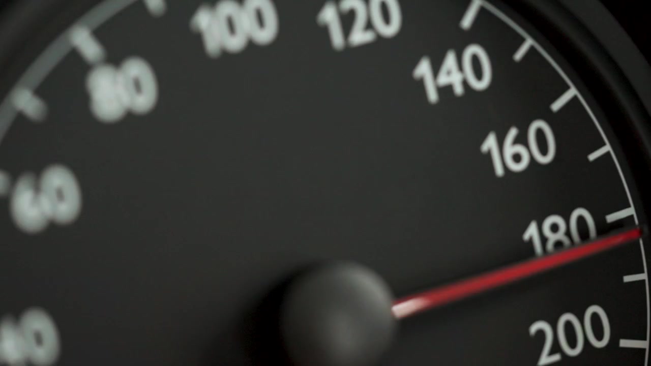 Close-up of a car speedometer with a red needle indicating high speed, with blurred blue police lights in the background. Concept image for speeding, traffic violations, police pursuit, emergency resp