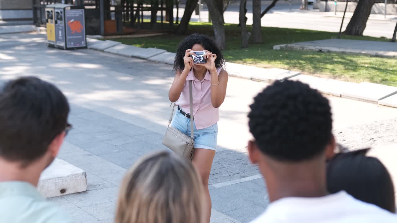 Donna che fotografa amici con una fotocamera digitale in una strada cittadina.
