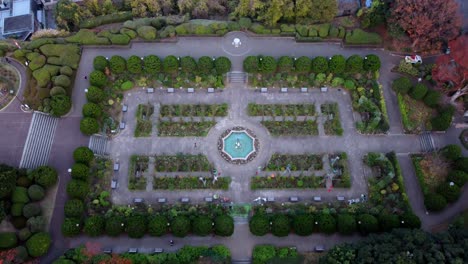 a symmetrically designed formal garden with a central fountain during autumn, aerial view