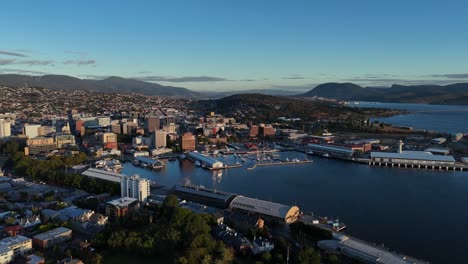 aerial establishing shot of hobart city with pier and port at golden sunset, tasmania