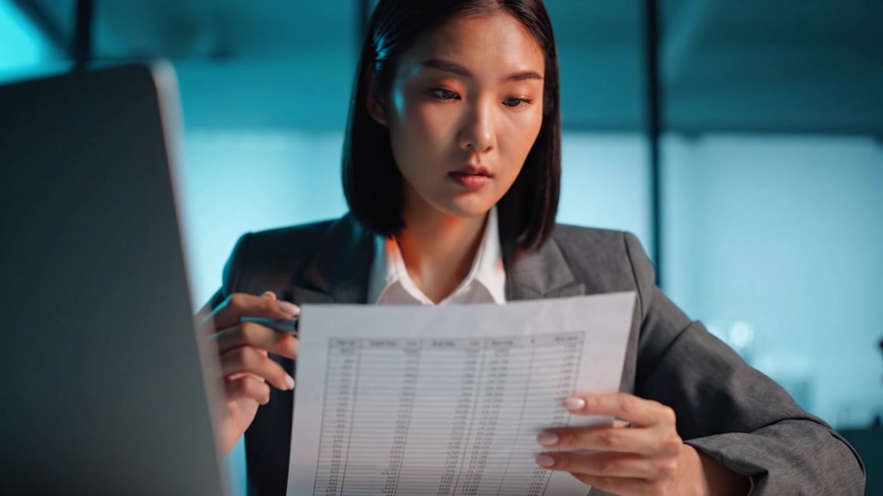 Focused Professional Reviewing Documents in an Office Environment with a Laptop, Emphasizing Concentration on Important Details and Responsibilities.
