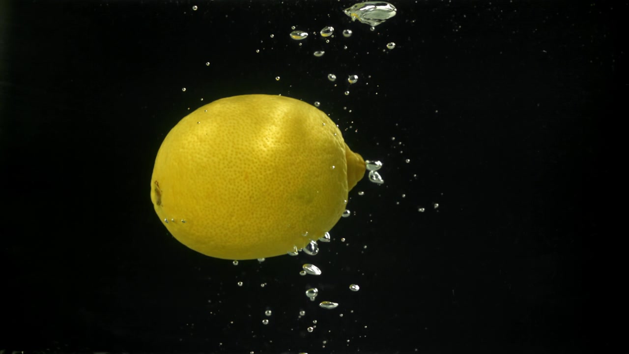 Limone giallo fresco immerso nell'acqua con bolle che salgono su sfondo nero.