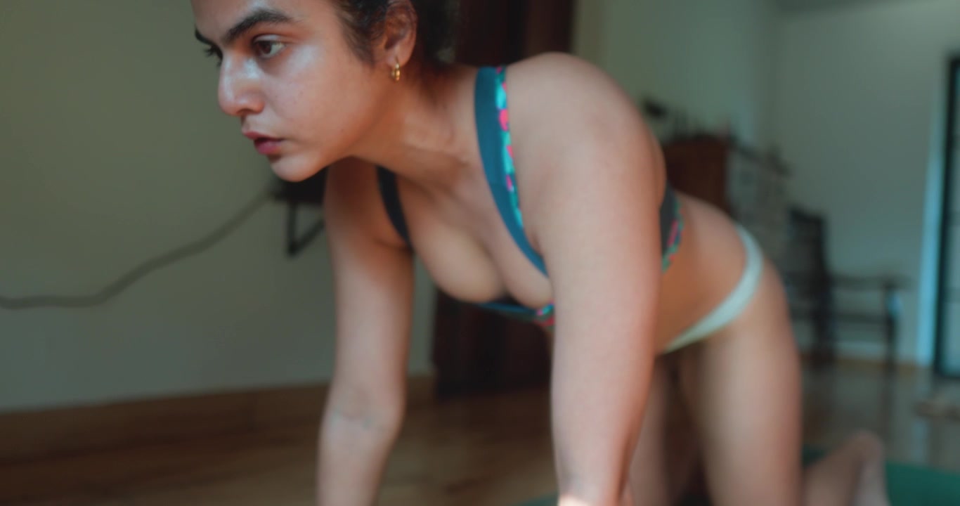 Primo piano di una donna che solleva la testa mentre mantiene un esercizio per il core in stile bear plank su un tappetino da yoga al chiuso.