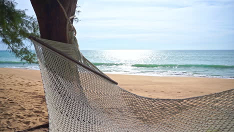 close-up of an empty woven hammock on a deserted beach overlooking the ocean waves