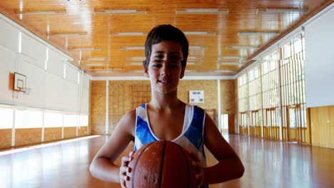 retrato de un escolar sosteniendo una pelota de baloncesto en una cancha de baloncesto