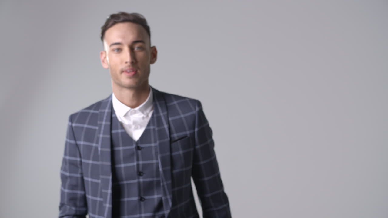 슈트 입은 웃는 남자가 카메라로 걸어가서 초점을 맞추고 돌아갑니다.