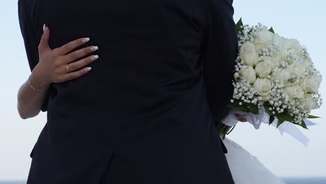 close-up of a bride and groom embracing as the wind gently blows her bouquet, no faces