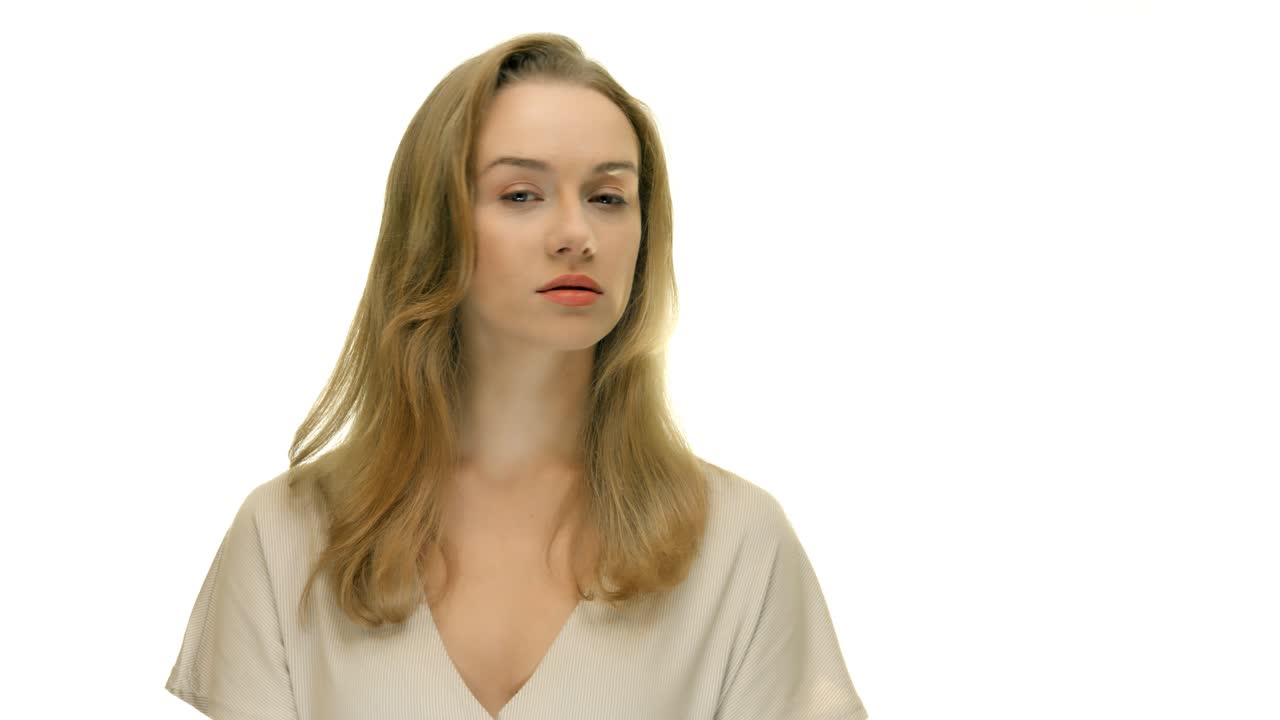 매끄러운 흰색 스튜디오 배경에서 먼 곳을 바라보고 있는 여성의 클로즈업, 그런 다음 카메라를 향해 머리를 돌립니다.