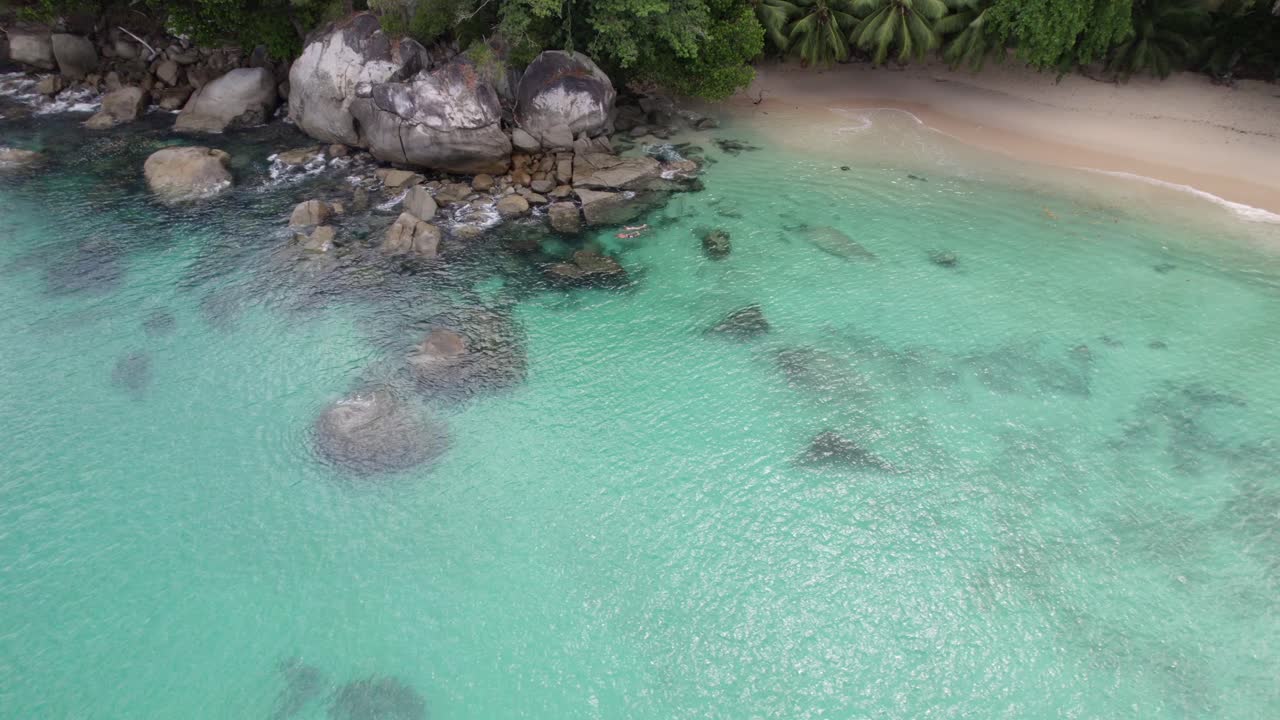 Filmato aereo della spiaggia di Sunset sull'isola di Mahé, coppia di turisti che fanno snorkeling vicino alle rocce, acqua cristallina, Mahé Seychelles 30fps 002
