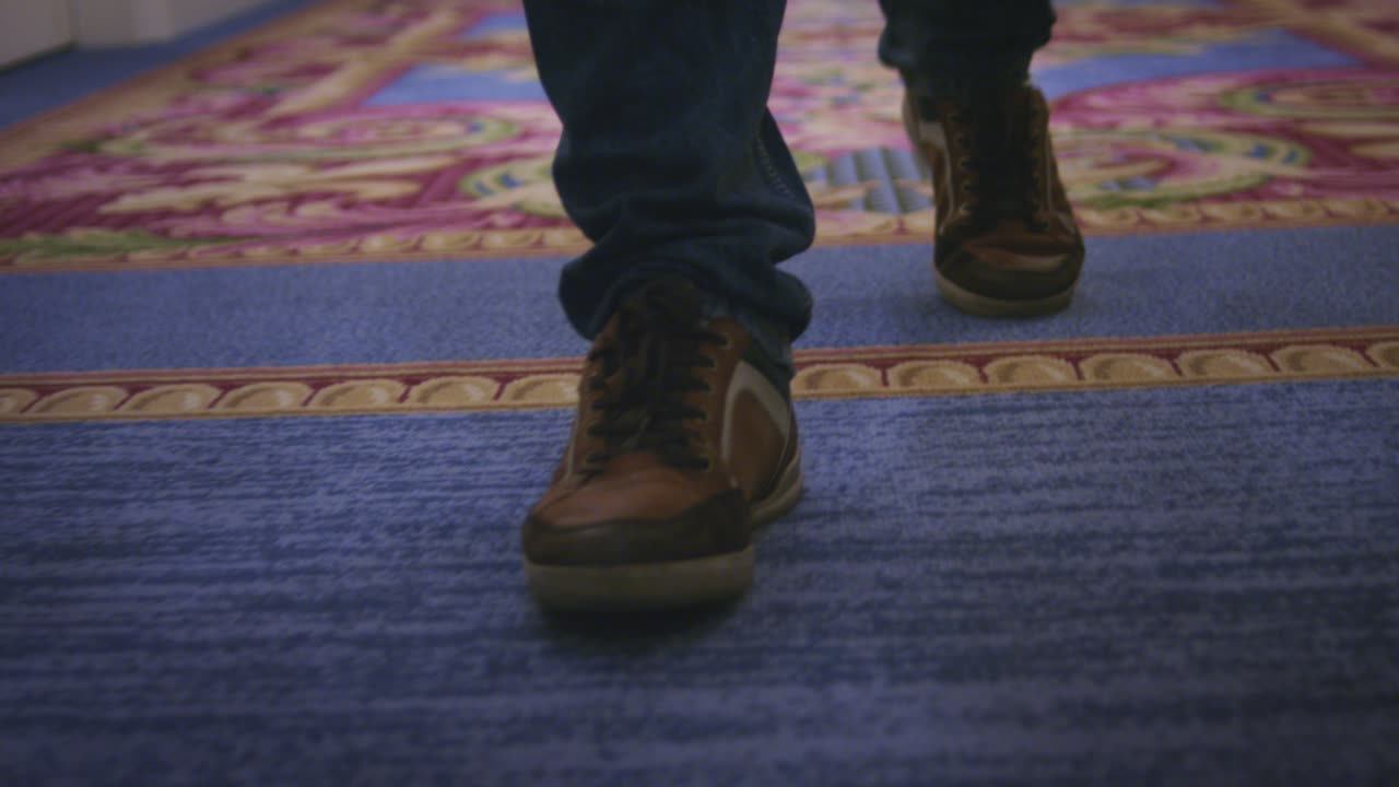 pies masculinos en zapatos deportivos caminando por el piso de la alfombra en el pasillo del hotel de huéspedes