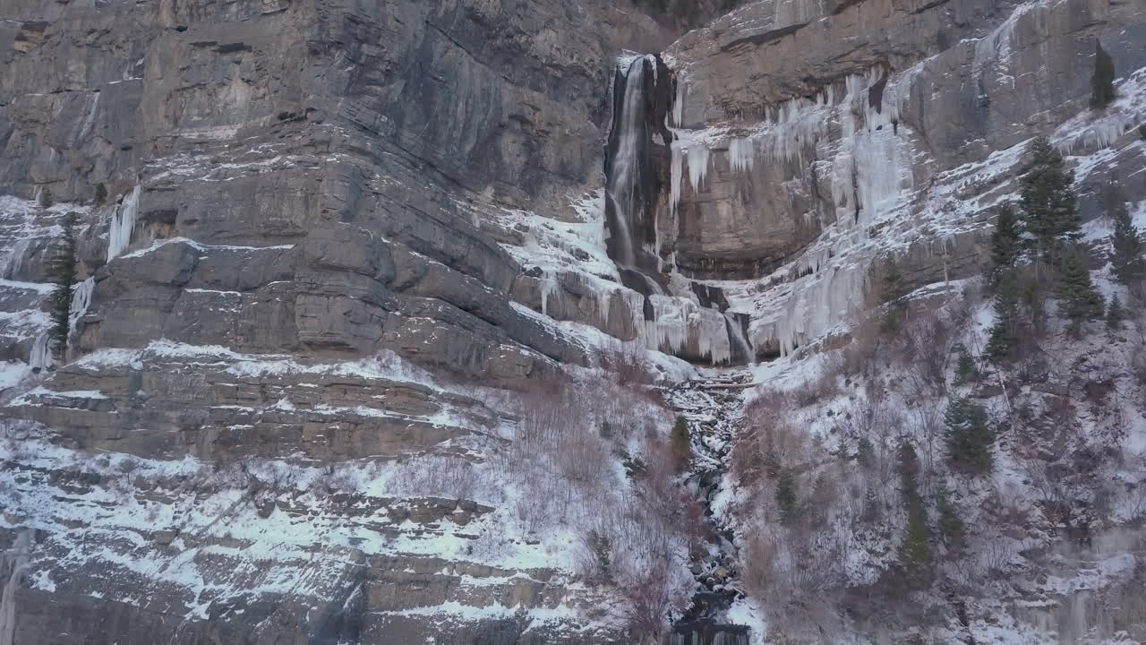 una hermosa cascada medio fluyendo y medio congelada en un terreno montañoso escarpado