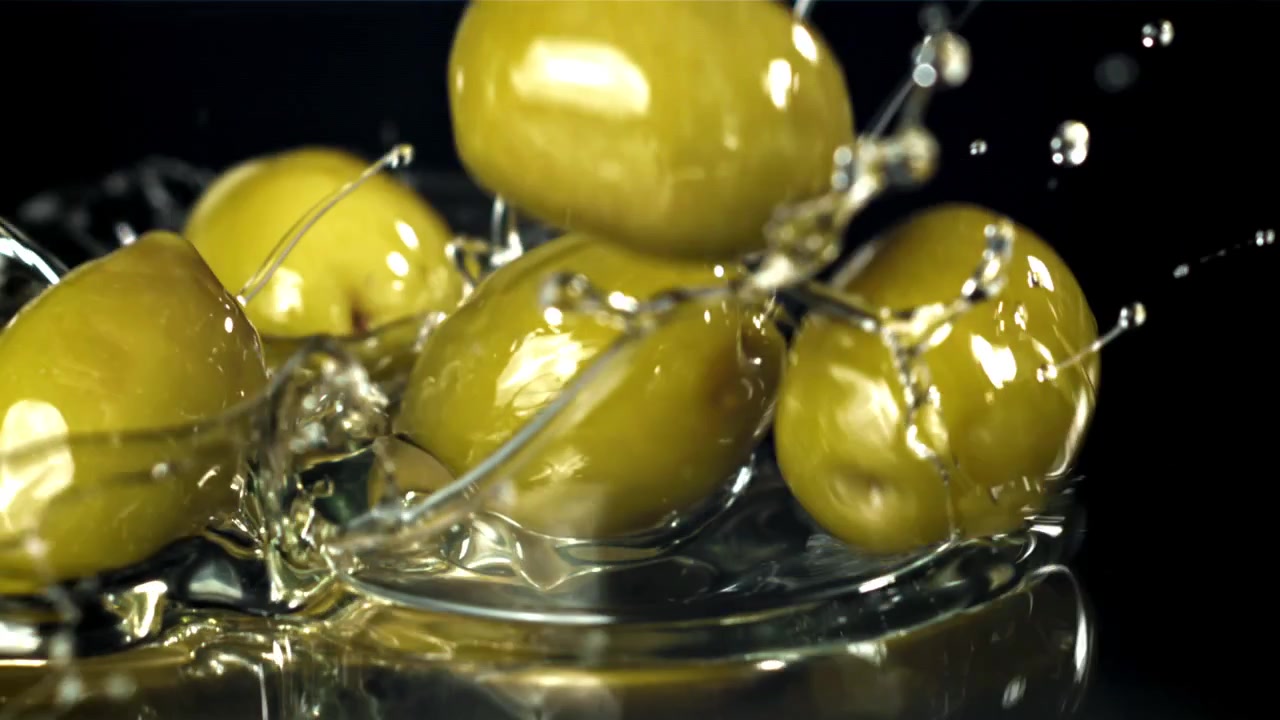 Olive verdi che schizzano nell'acqua al rallentatore.