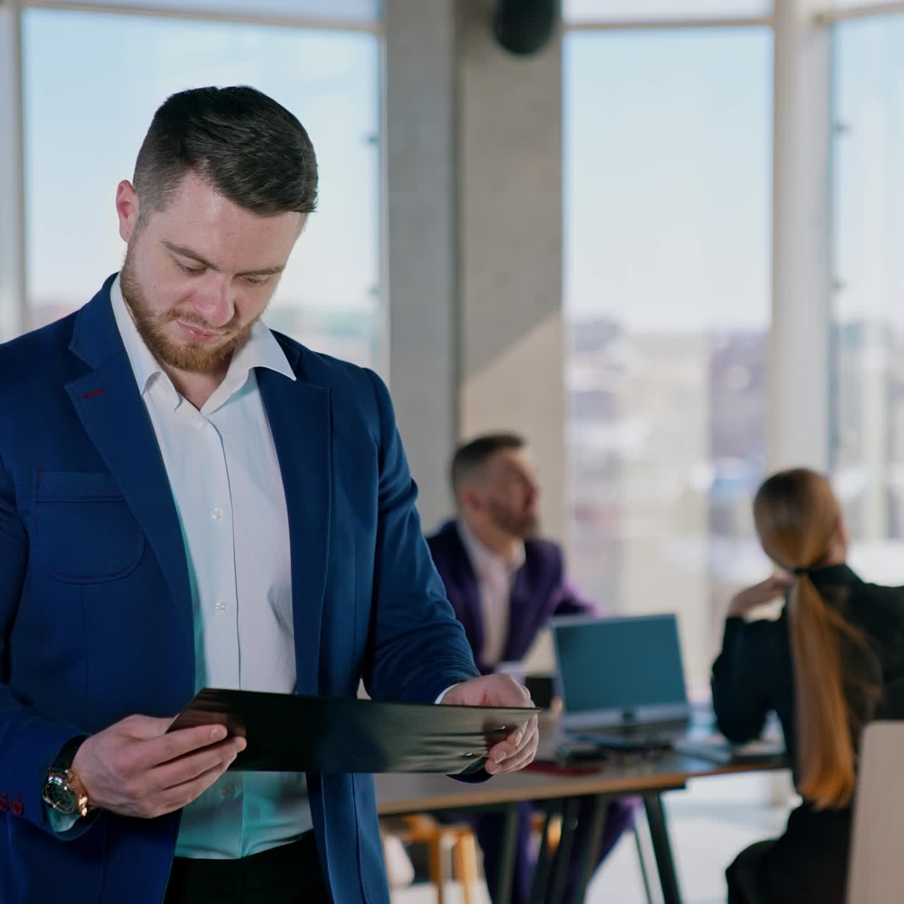 Young businessman with papers in office center. Portrait of a handsome bearded entrepreneur in white shirt and suit holds a folder and reading documents