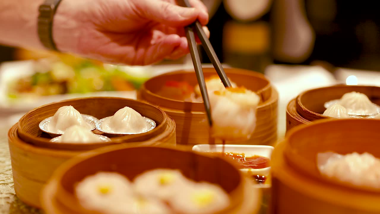 Chopsticks pick dim sum from bamboo steamers in a warm, inviting restaurant setting with soft lighting