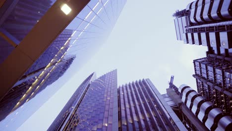 looking up at london skyscrapers downtown at dusk, clear sky and building lights with reflections, strolling in the city at night