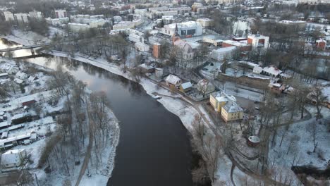 a breathtaking aerial view of valmiera city, showcasing the winding gauja river surrounded by snow-covered landscapes and residential areas under a wintry sky.