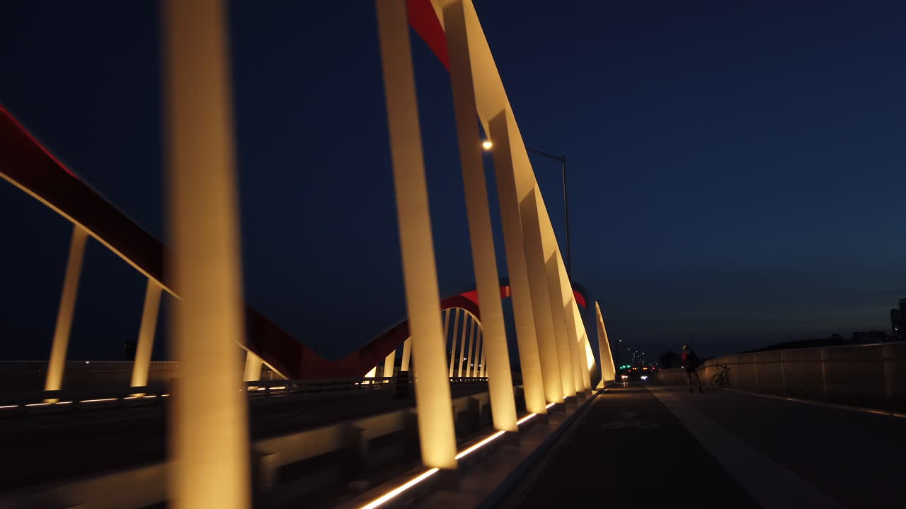 Night rider cyclist's point of view passing by a well lit commissioners street bridge at twilight, wide shot