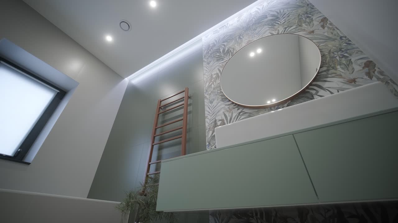 baño sofisticado con un acento de papel tapiz tropical, vanidad elegante, espejo redondo y iluminación ambiental