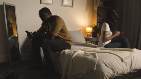 Couple-With-Relationship-Problems-At-Home-At-Night-Both-Looking-At-Mobile-Phones-In-Bedroom-3