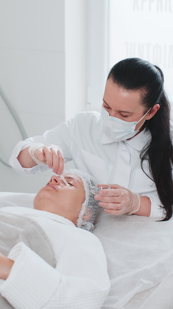 미용사는 여성의 눈 주변 피부에 보습성 질 산을 적용합니다. 노화 방지 치료