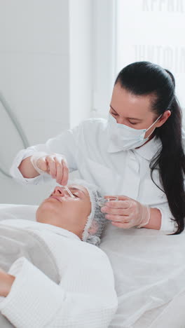 cosmetólogo aplicando ácido pelador hidratante en la piel alrededor de los ojos de la mujer tratamiento antienvejecimiento