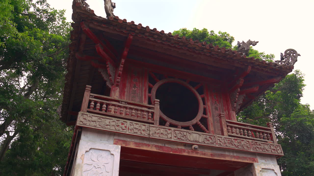 Sudut rendah dari Paviliun Khue Van Cac di Temple of Literature di Hanoi. Arsitektur kayu merah ikonis dengan jendela melingkar yang dikelilingi oleh pepohonan hijau di situs bersejarah Vietnam