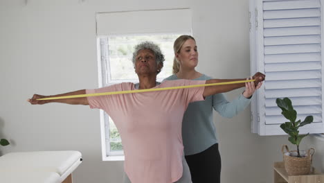 caucasian nurse with senior woman exercising with rubber band, copy space, slow motion