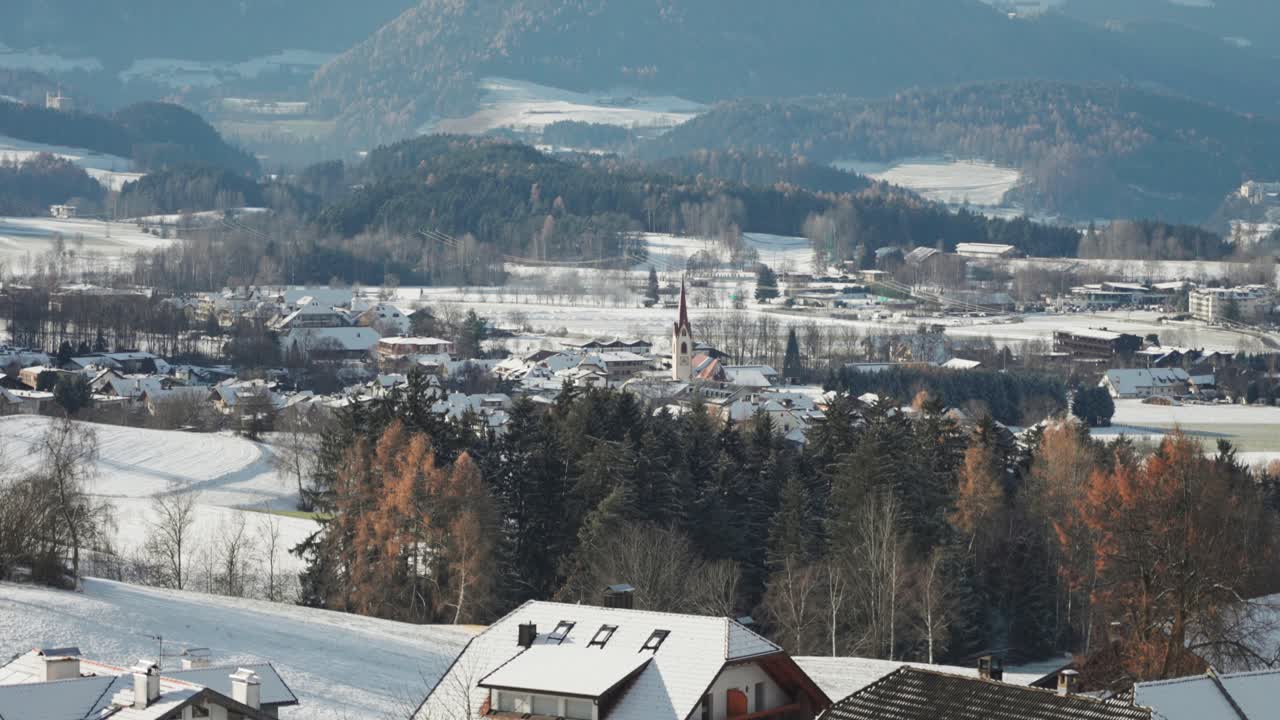 A peaceful South Tyrolean village rests in a snowy valley, with a church spire rising among rooftops.
