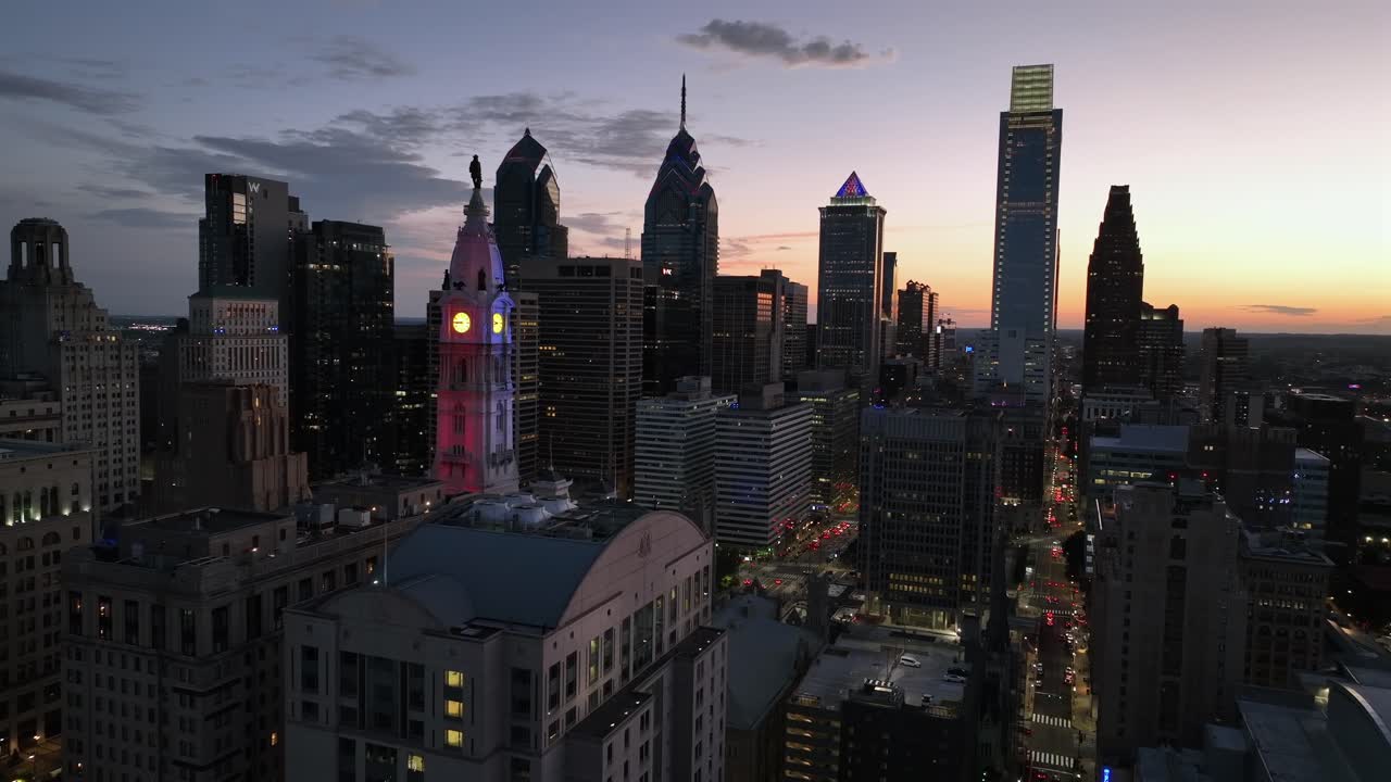 Aerial establishing shot of skyline of Philadelphia at golden sunset. City hall lighting in red, white and blue colors. Peaceful dusk scene in American metropolis. Skyscraper and high-rise buildings