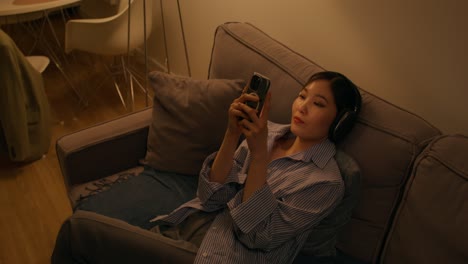 woman relaxing on couch with headphones and phone