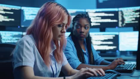 two women collaborate in a modern tech environment, engaged in coding and problem solving amidst bright computer screens displaying data and code
