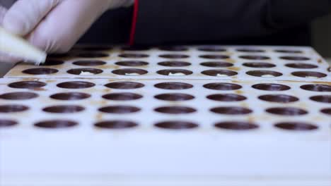 chocolatier pouring ganache filling into chocolate mold preparing candy
with a pastry bag