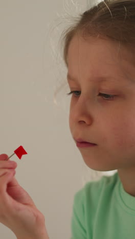 little girl with ponytail looks at pin with red flag intently spinning. tired schoolgirl takes break from doing homework sitting in light study room at home closeup