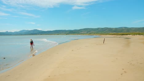 Frau-Am-Weißen-Sandstrand-Im-Seichten-Wasser-Mit-Bergkulisse---Weitschuss