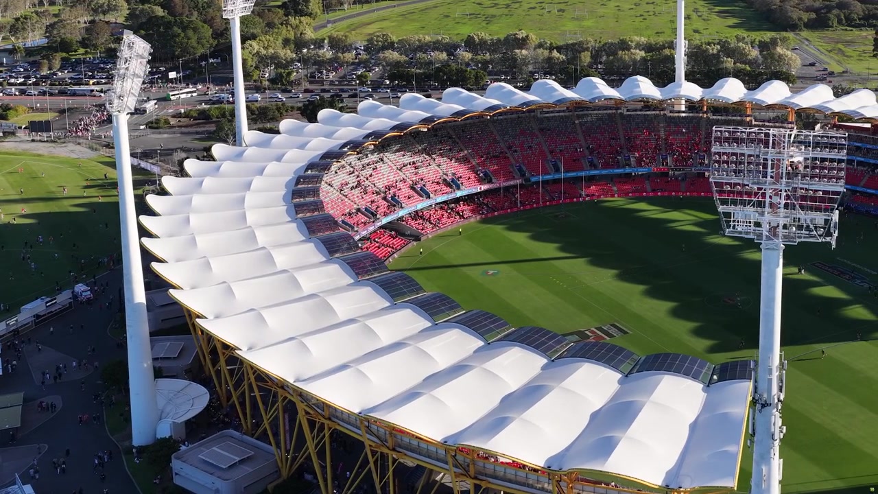 Droneopptak panorerer over et stort stadiontak og grønn idrettsbane i skarpt dagslys