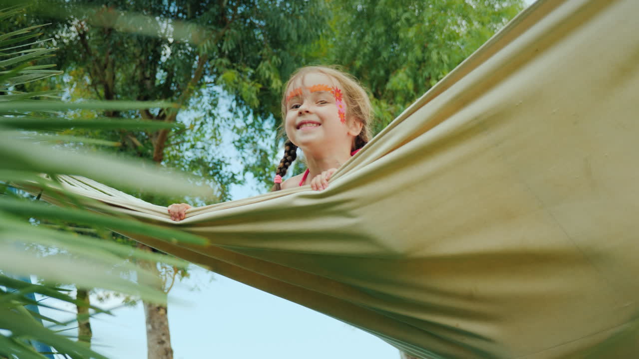 얼굴을 칠한 재미있는 아이들은 해변에 있는 호텔 영토에서 해먹을 타고 있습니다.