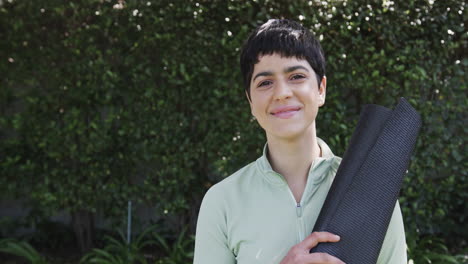 happy caucasian woman standing with yoga mat and smiling in sunny garden, copy space, slow motion