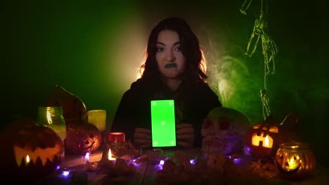 una mujer joven con manto negro está apuntando a la pantalla verde del teléfono inteligente