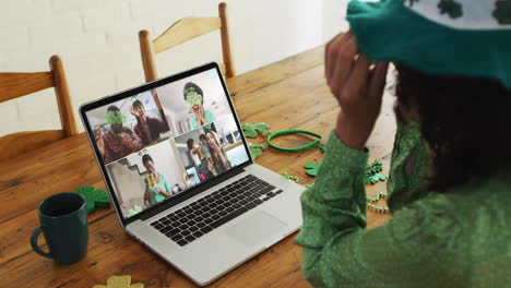 un grupo diverso de amigos sonrientes con cerveza vistiendo artículos en forma de trébol en una videollamada en una computadora portátil