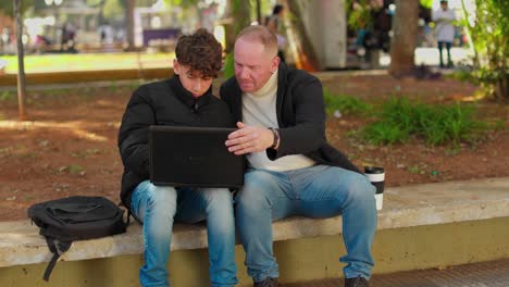 two men using a laptop together outdoors