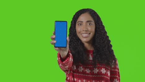 retrato de estudio de una mujer con un jersey navideño sosteniendo un teléfono móvil contra una pantalla verde 2