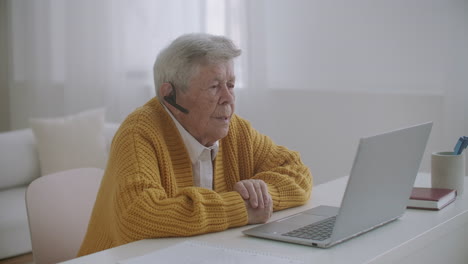 Mujer-Mayor-Con-Computadora-Portátil-Llamando-A-Un-Teléfono-Inteligente-En-Casa.-Anciana-Haciendo-Una-Videollamada-En-El-Portátil-Sonriendo-Y-Hablando-Alegremente-En-El-Interior-De-Un-Acogedor-Apartamento.-Doctor-Videollamada-Paciente-Mayor