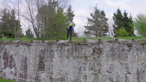 Stylish,-happy,-young-woman-waves-from-the-top-of-a-wall