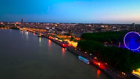 large ferris wheel lit up in neon lights with crowds in bordeaux france during wine fair, aerial pan right shot