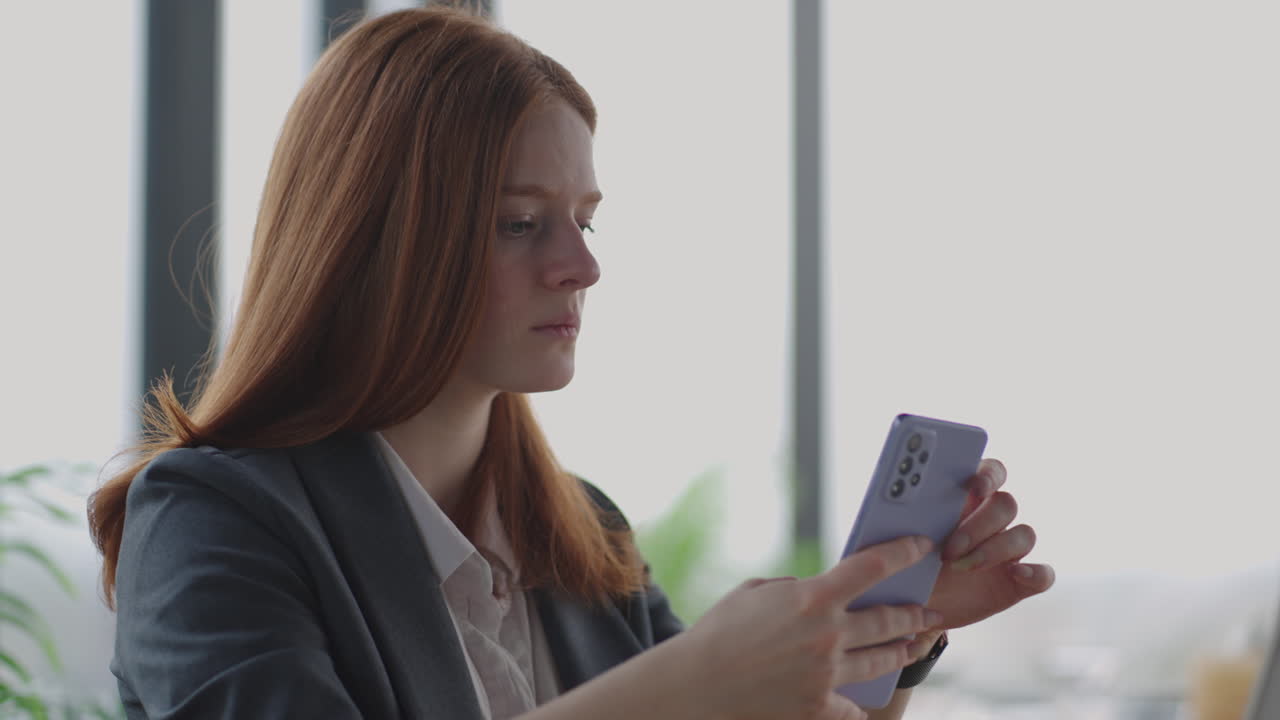 красивая молодая деловая женщина использует телефон в офисе. женщина использует смартфон и опирается на окно, отправляет текстовые сообщения, отправляет электронные письма, планирует встречи, создает сети в интернете, просматривает сообщения на мобильном телефоне